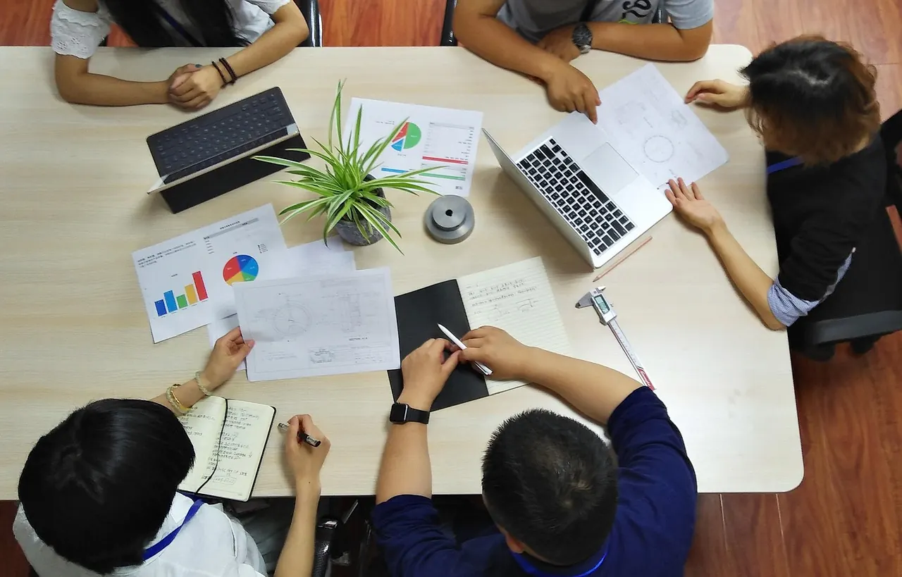 Nhóm người làm việc quanh bàn có laptop và tài liệu