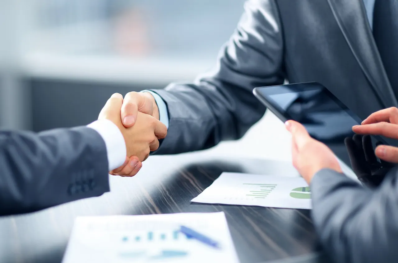 Hai người bắt tay trên bàn có tài liệu
