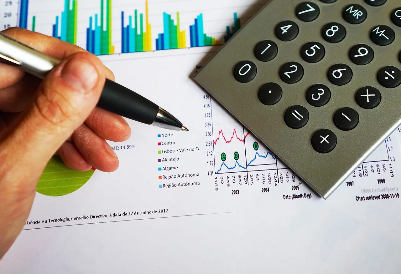Bàn tay cầm bút ghi chú bên biểu đồ in và máy tính cầm tay