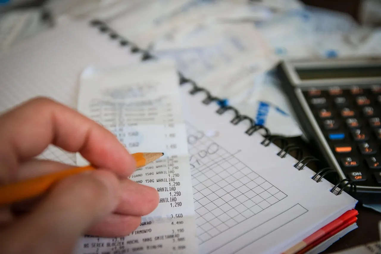 Bàn tay cầm bút chì rà soát từng dòng trên bảng số liệu