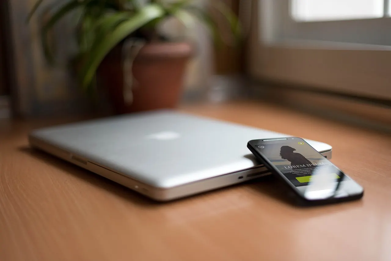 Laptop và điện thoại đặt cạnh nhau trên bàn gỗ