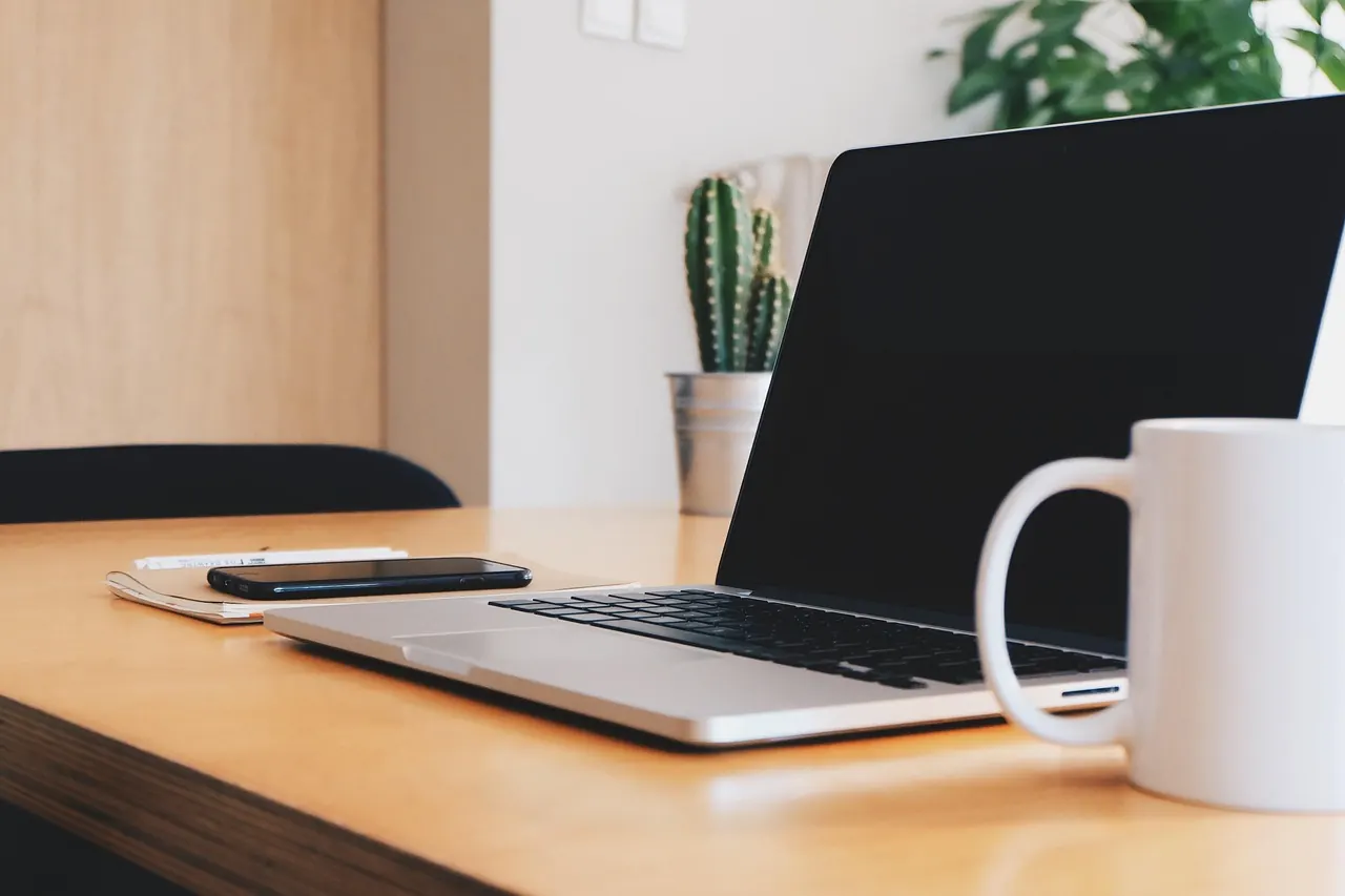 Laptop và cốc trắng trên bàn gỗ sáng